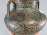 a hand holding a vase that has a handle on it