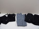 Plusieurs paires de vêtements noirs et gris sont disposées sur une table blanche