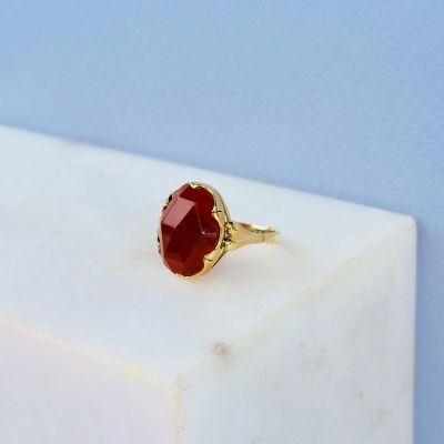 une bague en or sertie d'une pierre rouge, posée sur un bloc de marbre blanc