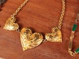 a gold necklace with a heart and a green bead on it