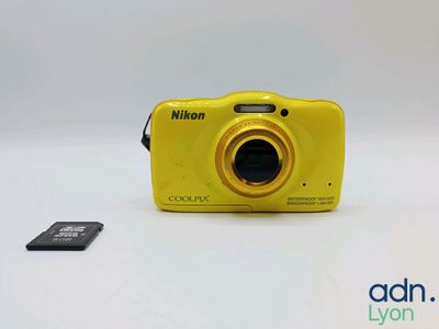 yellow digital camera sitting next to a micro sd card on a white surface
