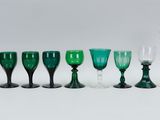 several green wine glasses are lined up on a white surface