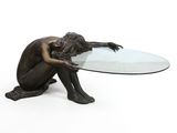 une statue en bronze représentant une femme assise sur une table en verre