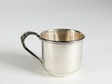 une tasse en argent avec une anse, posée sur une surface blanche