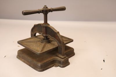 une presse ancienne en fonte avec une poignée en bois, posée sur une surface blanche