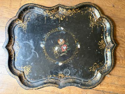 un plateau noir orné d'un motif floral, posé sur un parquet