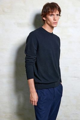 the man is standing in front of a white wall wearing a black sweater and blue pants
