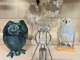 Plusieurs chouettes en verre sont posées sur une étagère à côté d'un bougeoir.