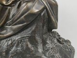 bronze statue of a woman sitting on a rock with her hand on her chin
