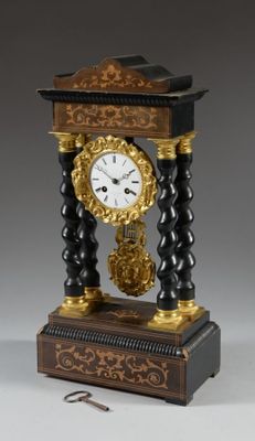 une horloge noire et dorée posée sur un socle, avec une clé