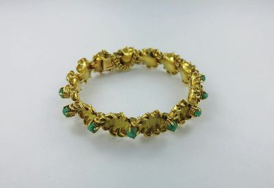 un gros plan sur un bracelet en or orné de pierres vertes