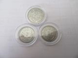 three silver coins in plastic containers sitting on a white surface