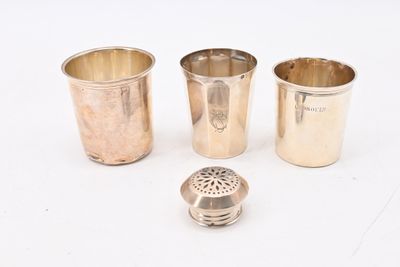 trois tasses en argent et une passoire en argent posées sur un plan de travail blanc