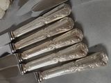 five silver knives and a knife holder on a table