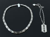 un collier composé de deux pièces d'argent et une lame de rasoir posés sur une surface noire
