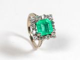 an emerald and diamond ring on a white surface