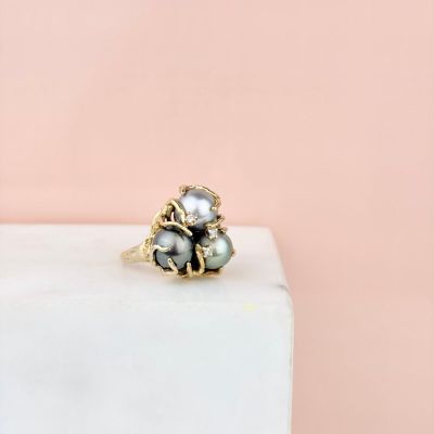 un gros plan d'une bague en or ornée de perles, posée sur un bloc de marbre