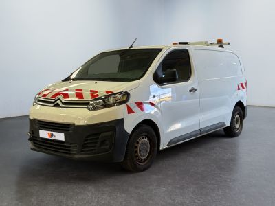 La camionnette blanche est garée dans une grande pièce ; elle porte une bande rouge et blanche sur le côté.