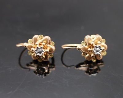 une paire de boucles d'oreilles en or et diamants posées sur un fond noir