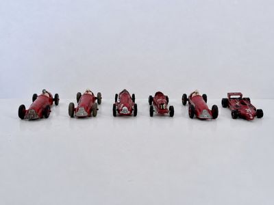 six petites voitures rouges alignées sur une surface blanche