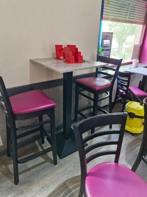 tables and chairs in a restaurant with pink chairs and a yellow trash can