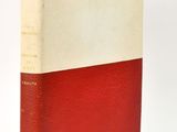 an old red and white book sitting on top of a white surface