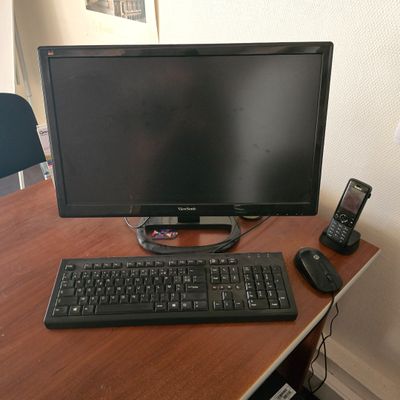 un écran d'ordinateur et un clavier posés sur un bureau, à côté d'un téléphone