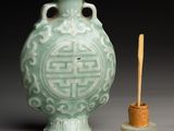 a green vase with a wooden stick in front of it