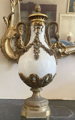 un vase blanc et doré posé sur une table, avec un miroir en arrière-plan
