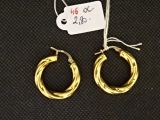 une paire de boucles d'oreilles créoles en or avec une étiquette de prix sur fond noir