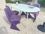 a white table with purple chairs and a bowl of fruit on it
