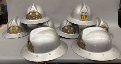 six casques de pompier blancs ornés de décorations dorées, posés sur une table