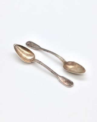 two silver spoons sitting on top of each other on a white surface