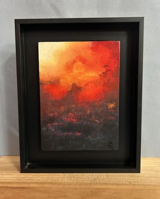 un tableau représentant un coucher de soleil orange et rouge dans un cadre noir