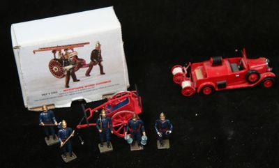 un camion de pompiers rouge en jouet et quelques figurines posées devant une boîte