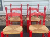 four red wooden chairs with wicker seats in front of a white house