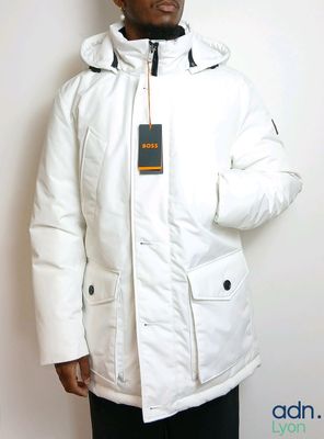 man wearing a white jacket and black pants standing against a white wall