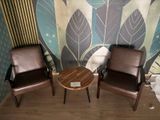 two chairs and a table in front of a wall with leaves