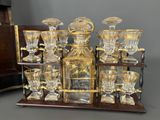 bottles and glasses on a wooden stand with a clock in the background