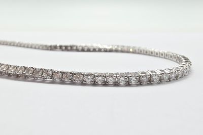 un gros plan d'un bracelet « tennis » en diamants posé sur une surface blanche