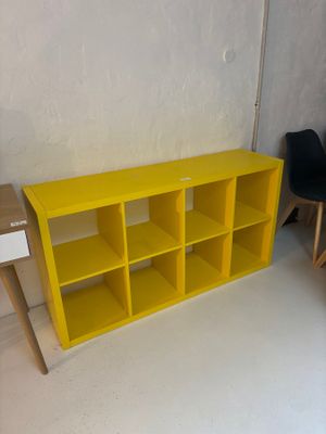 une bibliothèque jaune avec deux chaises noires à côté