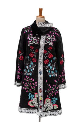 un manteau noir orné de fleurs et d'oiseaux colorés, présenté sur un mannequin
