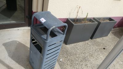 une poubelle posée à l'extérieur d'un immeuble, à côté d'un bac à fleurs