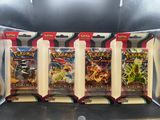 Quatre paquets de cartes à collectionner Pokémon se trouvent dans une vitrine.