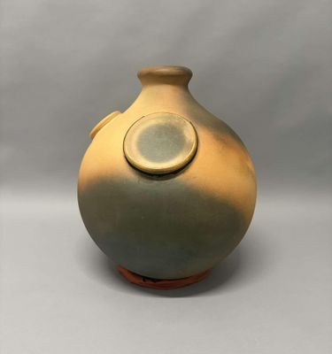 un vase marron avec un couvercle vert posé sur une surface blanche