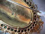 a close up of a gold brooch with green stones on it