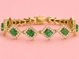 a gold bracelet with emerald stones and diamonds on a pink background