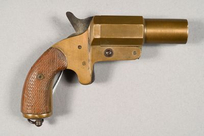 un vieux revolver en laiton avec une crosse en bois, posé sur une surface blanche