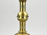 une lampe à huile ancienne en laiton posée sur un socle, sur fond blanc