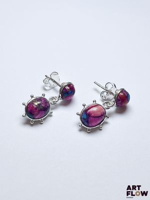 une paire de boucles d'oreilles en pierre rose et violette posées sur un fond blanc